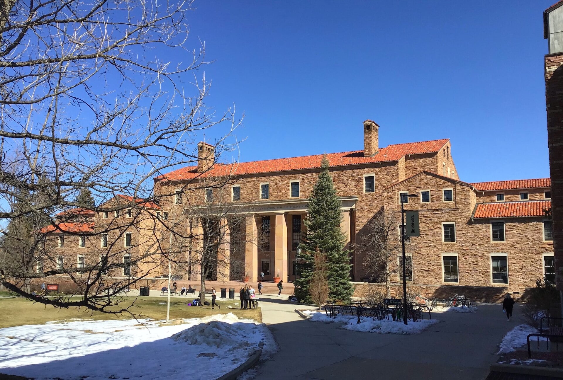 The sandstone walls and red tile roof of Norlin Library at the University of Colorado Boulder, with patches of snow on the lawn