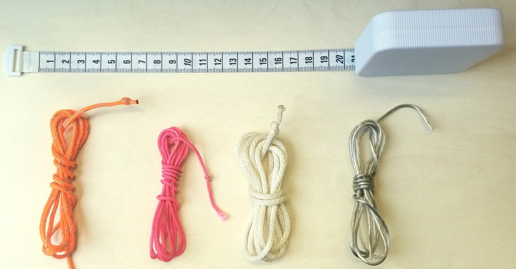 The four measuring implements, with a tape measure for scale: orange, pink and white braided polyester strings and a length of loudspeaker wire.